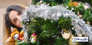 woman peering out from behind a christmas tree to illustrate an article on winter holiday stress