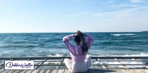 a woman taking deep breaths of clean air on the coast to illustrate an article about breathing exercises