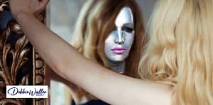 woman wearing a mask looking into a mirror to illustrate an article on imposter syndrome