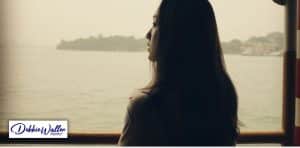 a woman alone staring through a window at a seascape to illustrate a article on loneliness