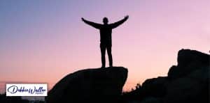 a person stood on a rock silhouetted against sunrise to illustrate an article on mind hacks to improve confidence