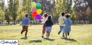 children with balloons running through a park to illustrate an article on stress free summer holiday activities